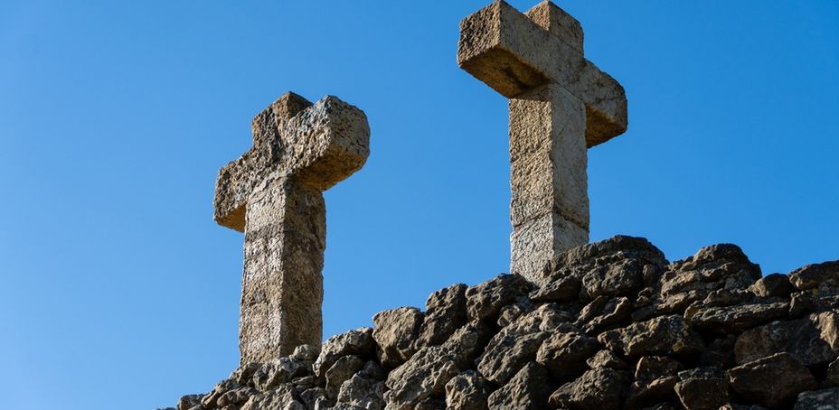 Two stone crosses standing tall against a clear blue sky with a rocky foreground.