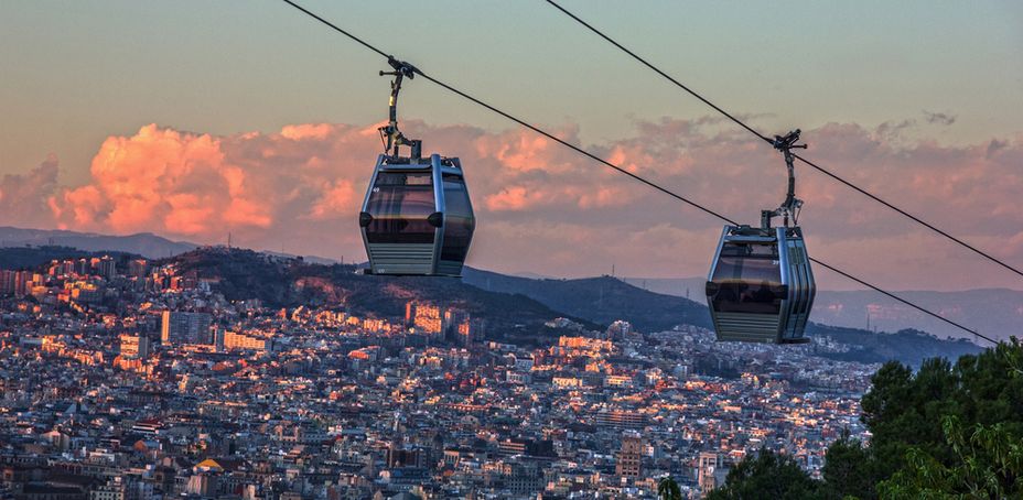 Cable car gondolas suspended over a vibrant cityscape, viewed from the top of Montjuic Hill in Barcelona.