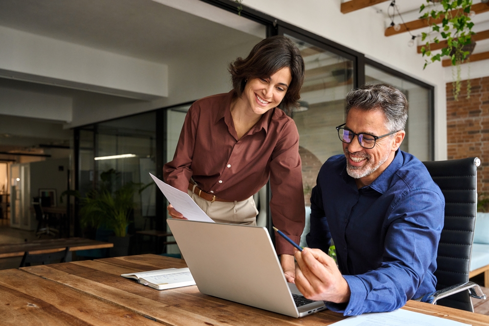 Two colleagues smiling and collaborating over a laptop at the office