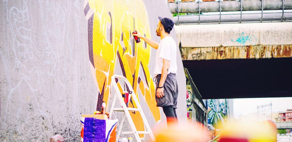 Street artist painting a colorful graffiti on a grey wall under bridge