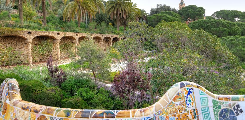 Colorful mosaic dragon sculpture and historic bridge at Park Guell in Barcelona.