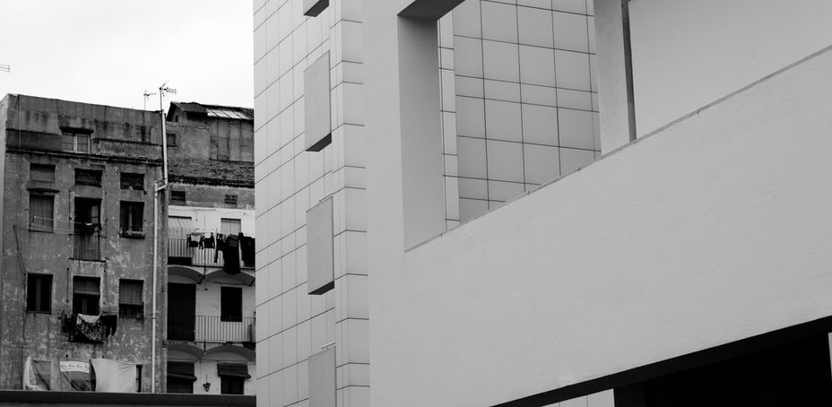 MACBA's modern building with its minimalist façade stands out from traditional buildings in an urban environment.