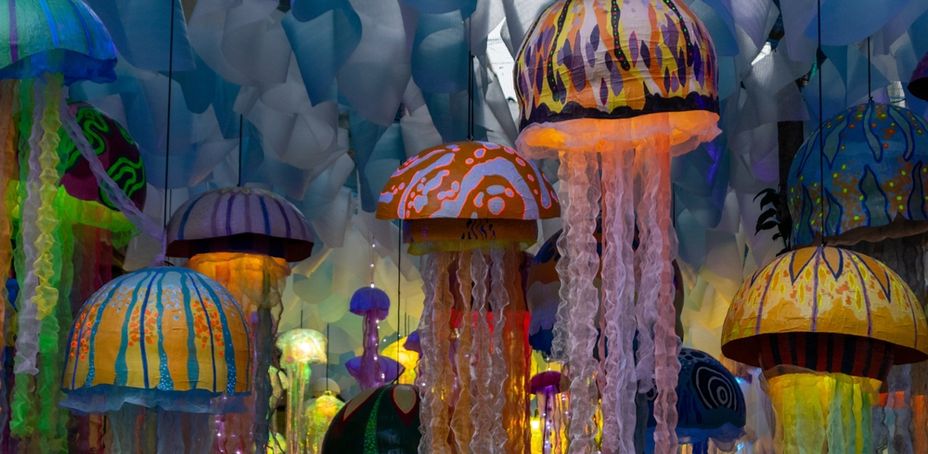 Colorful jellyfish sculptures hanging in an art installation, illuminated with vibrant lights.