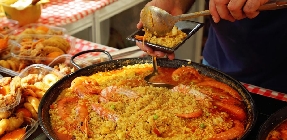 A person serving paella with shrimp and rice from a skillet at a restaurant in Barcelona.